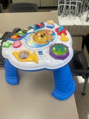 small activities table with blue legs.  Table has multiple activities include piano keys, horn, and other soundsn