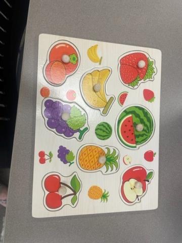 Wood puzzle with eight different fruits including an orange, a strawberry, a banana, a grapes, a watermelon, a pineapple, an apple, and a cherry. All fruits pieces have a wood peg for easy lifting.