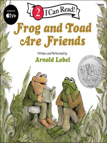 frog and toad sitting in grass with toad holding a book reading to frog