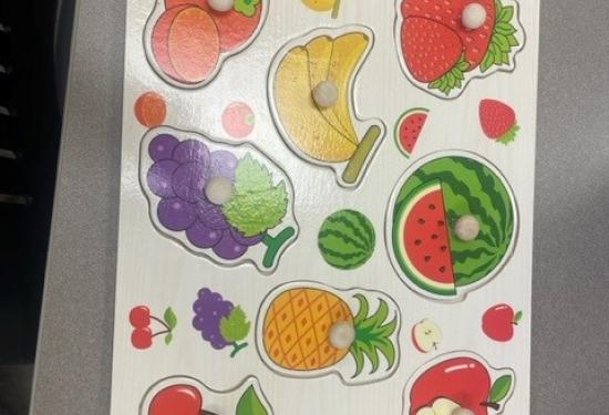 Wood puzzle with eight different fruits including an orange, a strawberry, a banana, a grapes, a watermelon, a pineapple, an apple, and a cherry. All fruits pieces have a wood peg for easy lifting.