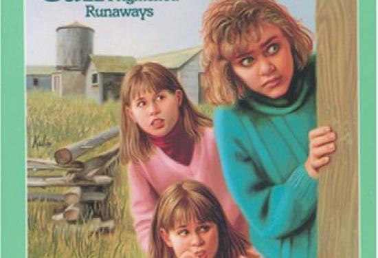 Three young girls peaking around a corner of a fence with a field in the background